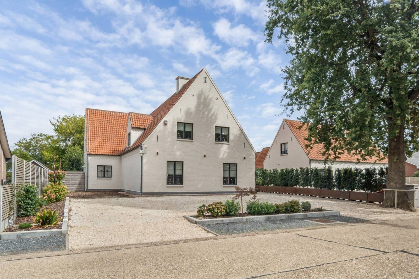 Een witte villa met verzorgde voortuin, verkocht door Mano Immo